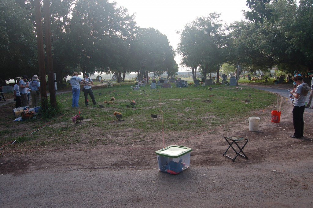 An area of the cemetery with small burial markers and string layed out by the team with team members surveying around