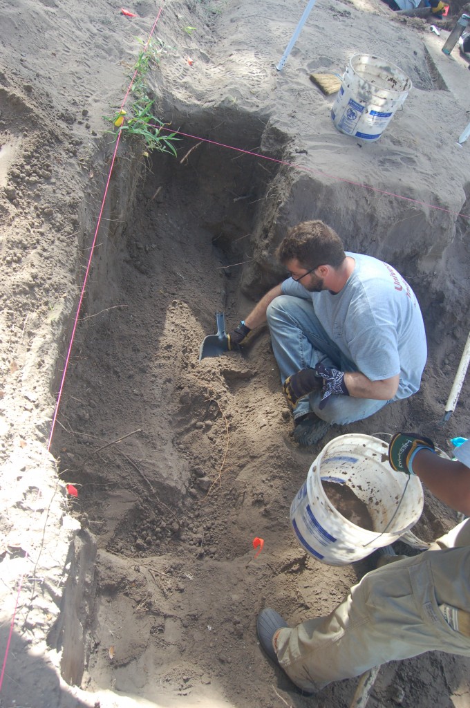 Justin removing burial fill with a dustpan from inside of a burial