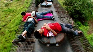 Children laying on metal grating with a moving background of brush