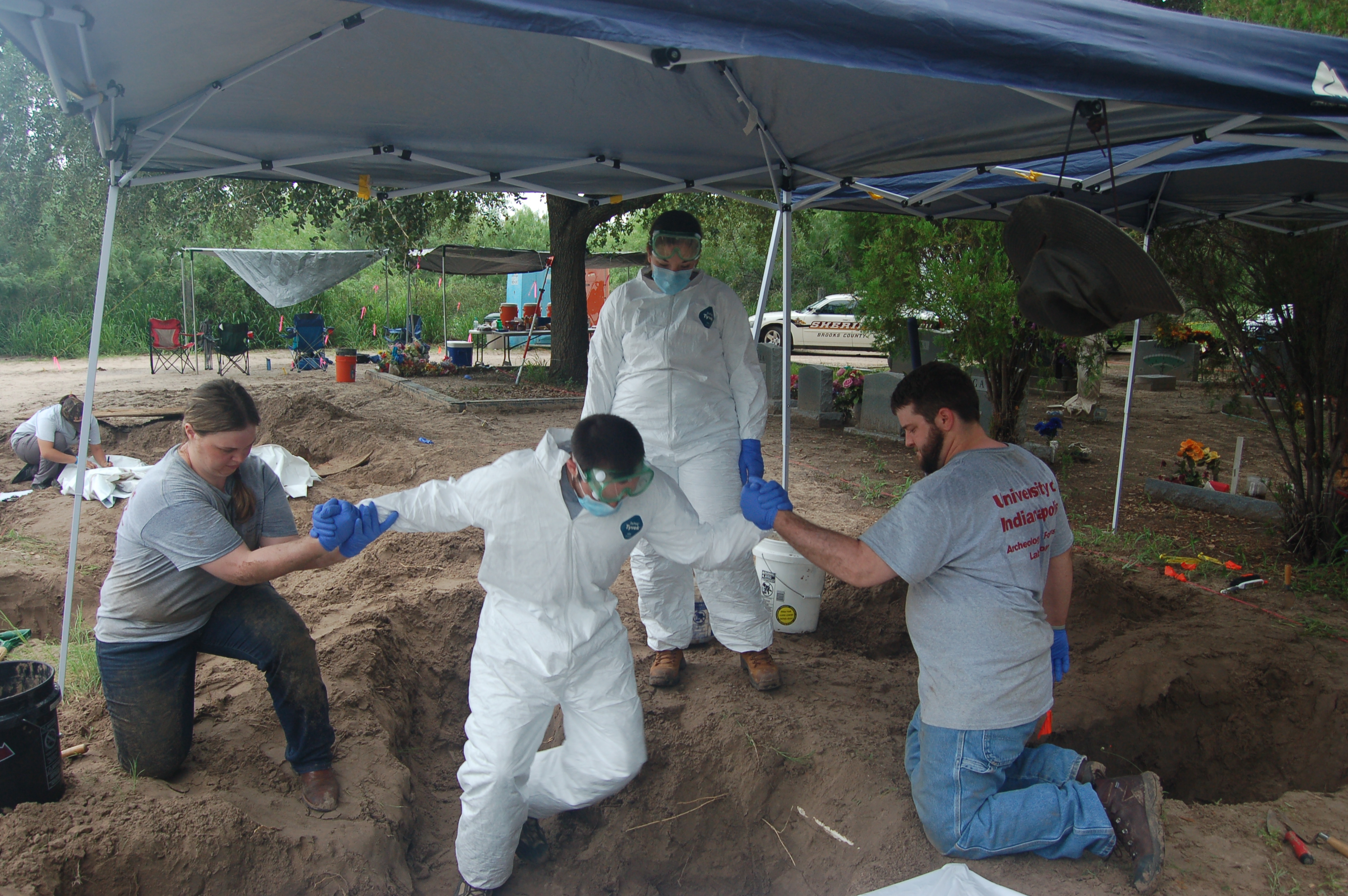 Beyond borders team members helping another member who is in full PPE head to toe into a burial