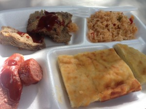 Arturos Dinner on a white styrofoam plate with different sections, rice, sausage, bread, and more meat