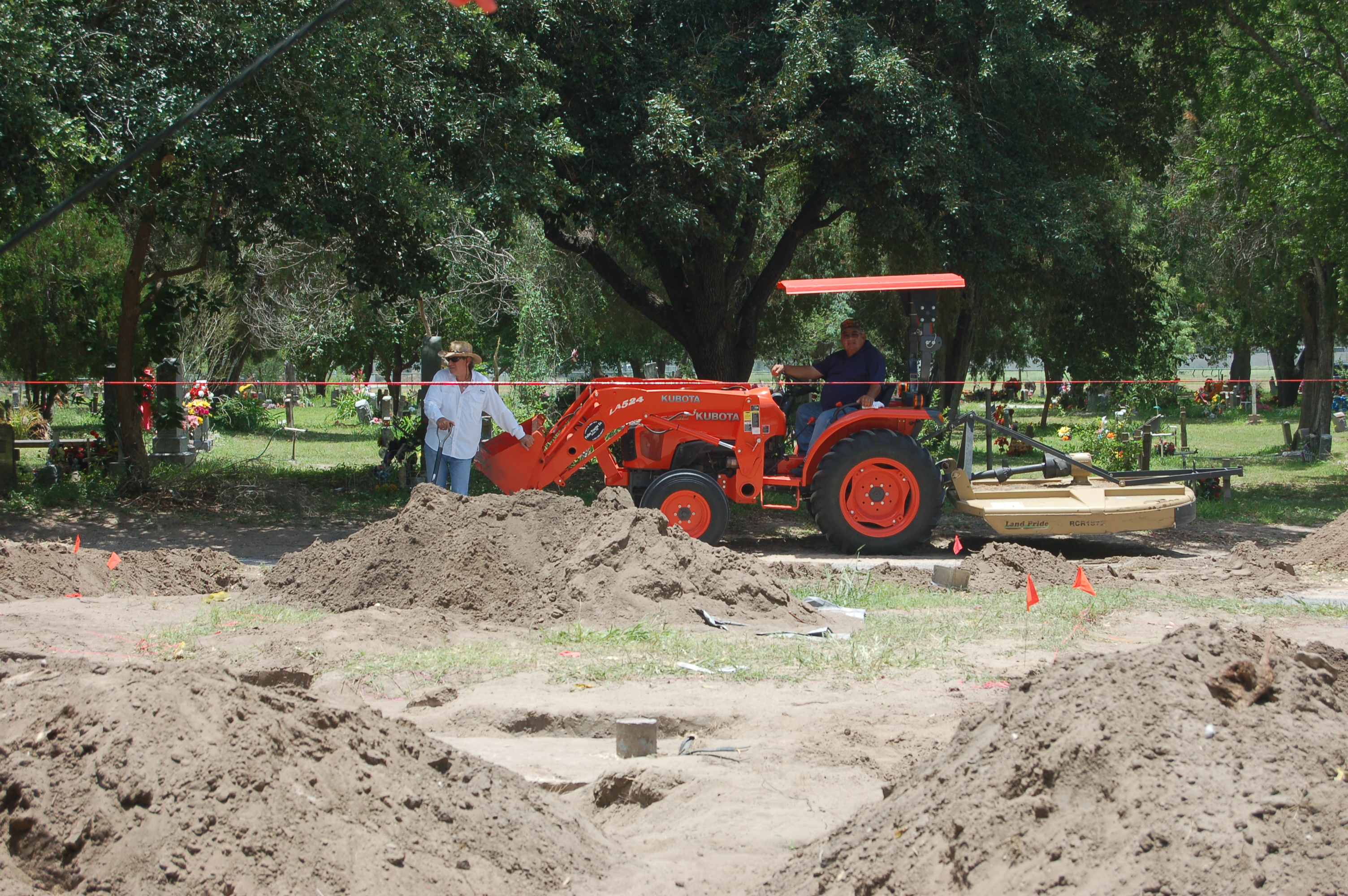 Large red backhoe in the distance behind multiple mounds of dirt