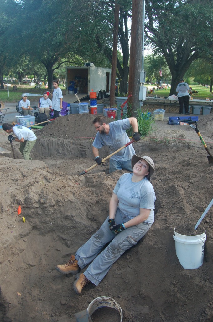 Burials being worked on with shovels while other team members sit in the background and Erica sits front and center