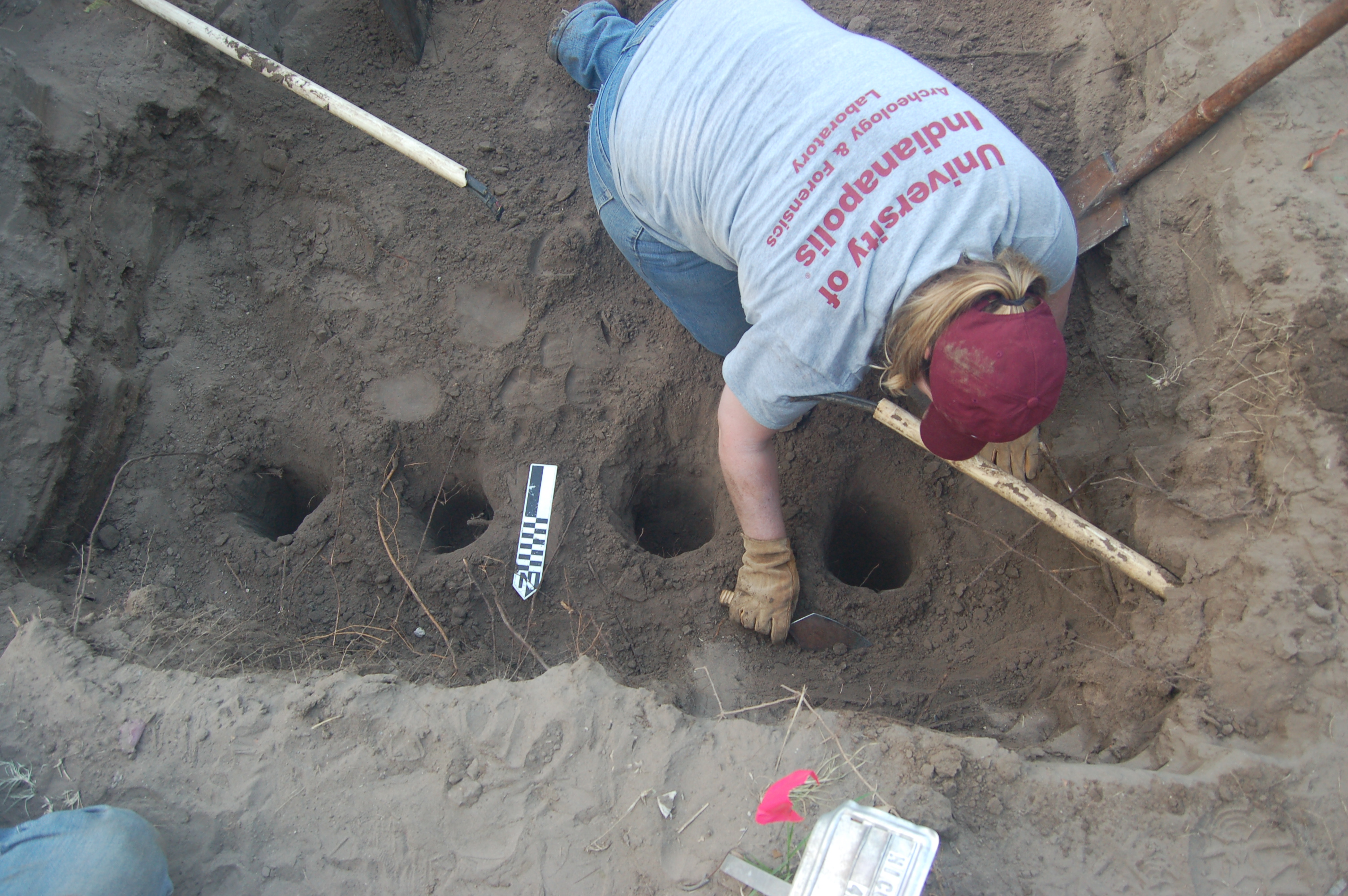 UIndy Team member using a trowel in a burial with 4 circular test pits dug