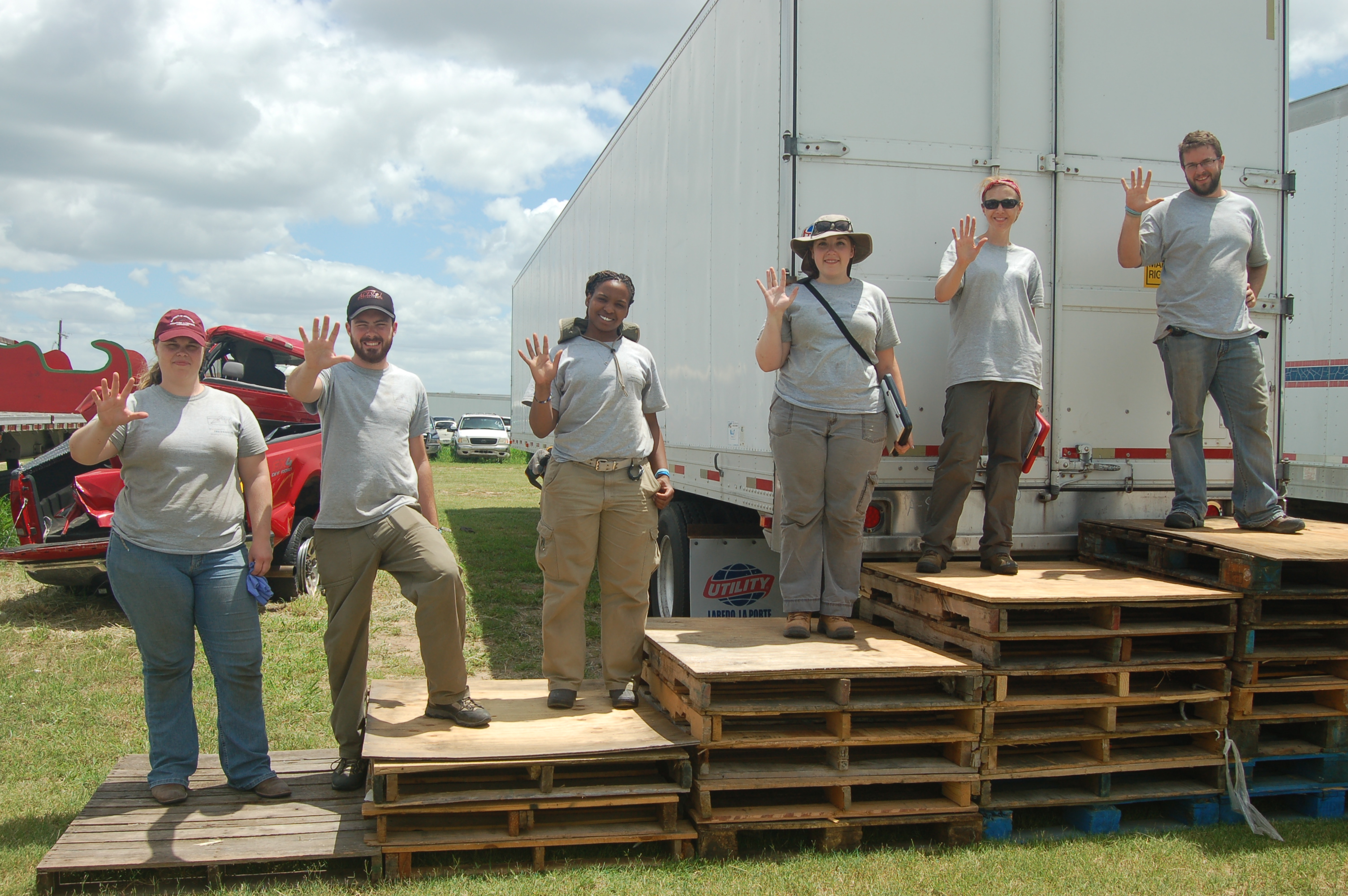 UIndy team holding up 5 fingers for day 5 while standing on increasing amounts of wooden palettes