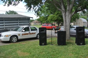 The constable vehicle in the background with large speakers and a microphone set up in front