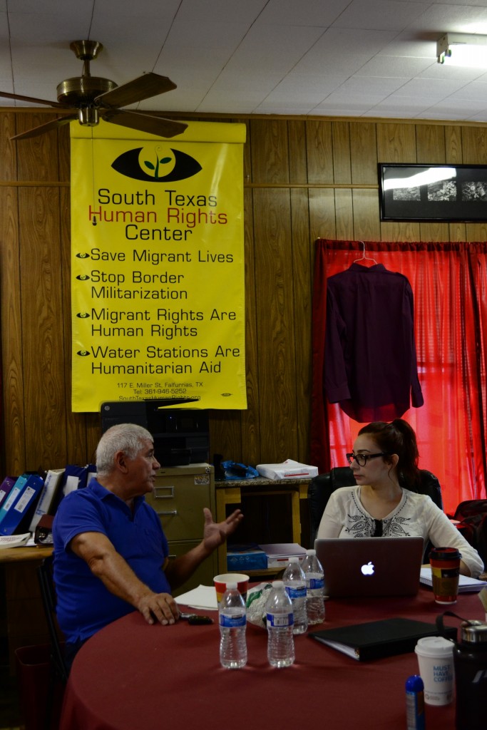 Director of the South Texas Human Rights Center, Eddie, engaged in a discussion with Priscilla in front of a South Texas Human Rights Center poster in the center