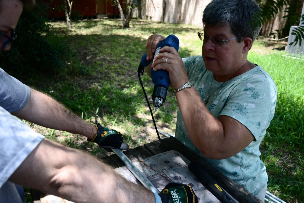 Sister Pam with a drill showing Justin how to build flag poles for water stations