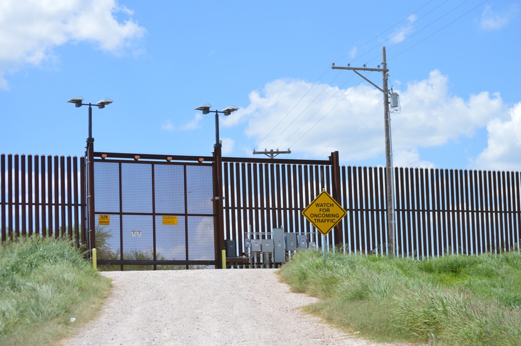 The border wall with a hazard sign outfront stating "Watch for oncoming traffic"