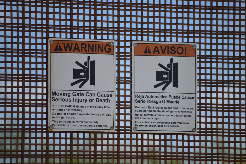 Warning signs in English and Spanish stating "Warning Gate can cause serious injury or death"