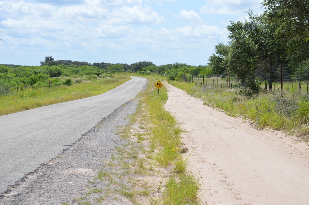 A paved road bordered by a dirt maintenance road