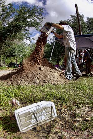 A team member dumping a bucket of dirt with an unknown remains burial marker closer to the camera