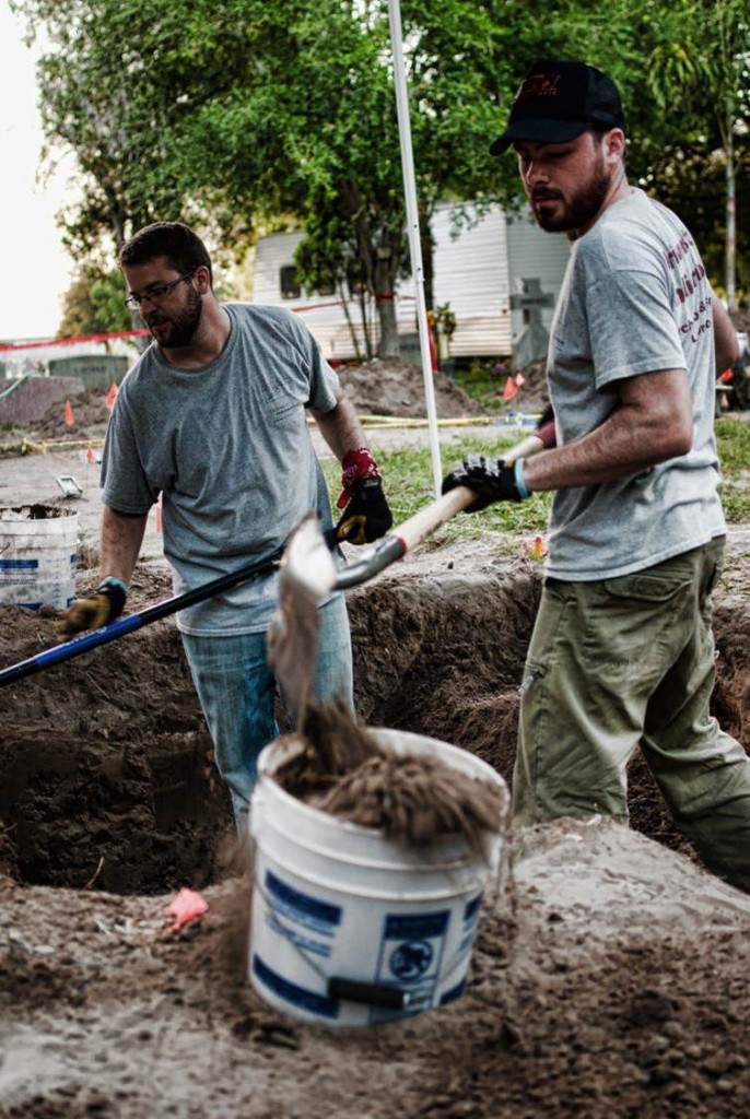 Justin and Ryan standing in a burial using shovels to scoop out burial fill