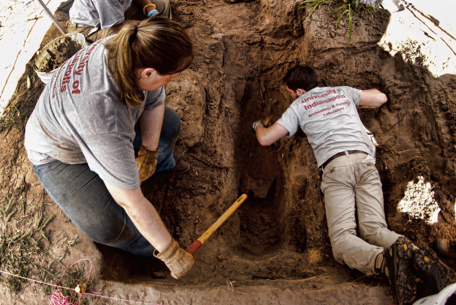 Jessica holding a shovel in a burial as Ryan lay deeper in the burial removing dirt