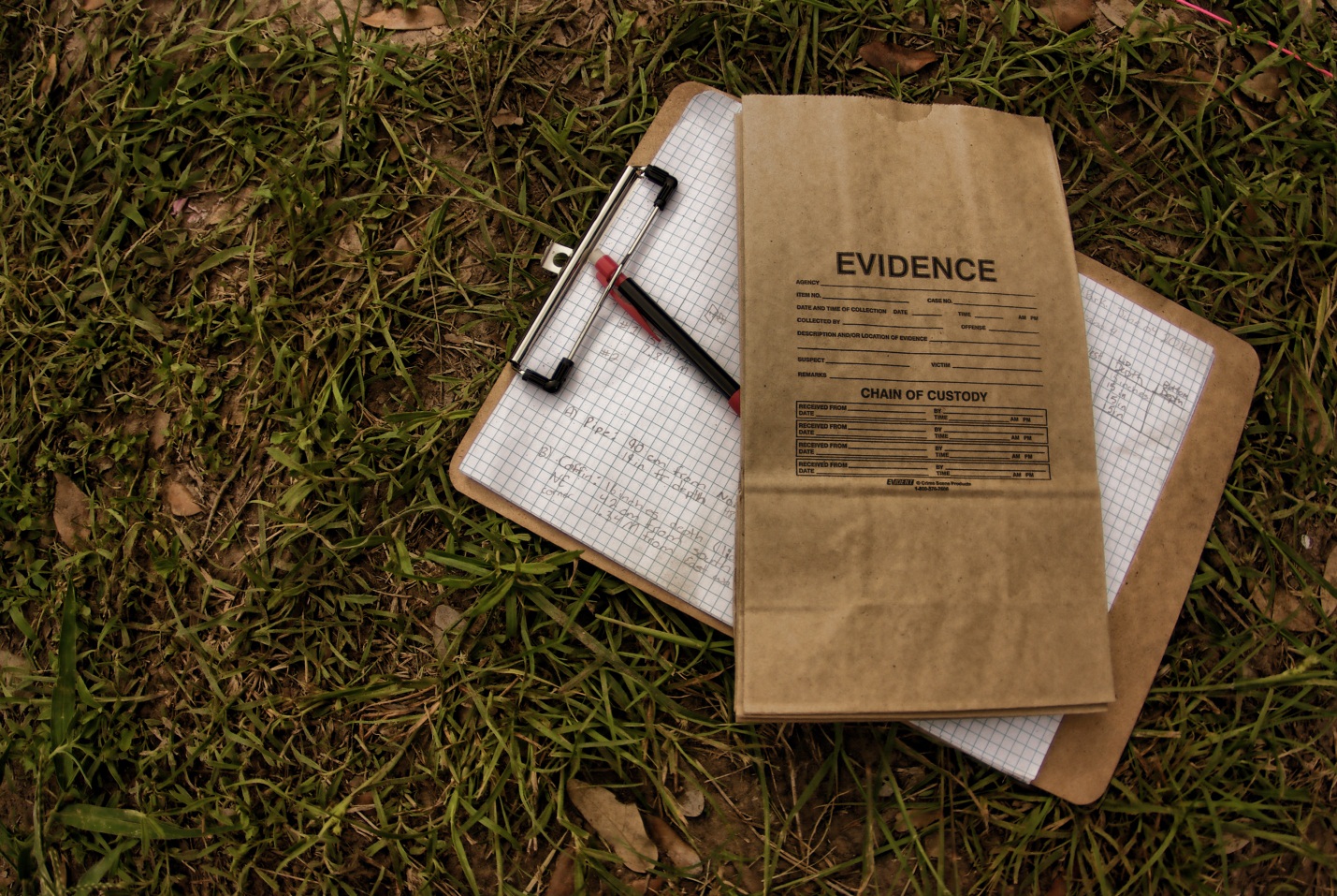 a brown evidence bag on a clipboard with a pencil and graph paper attached