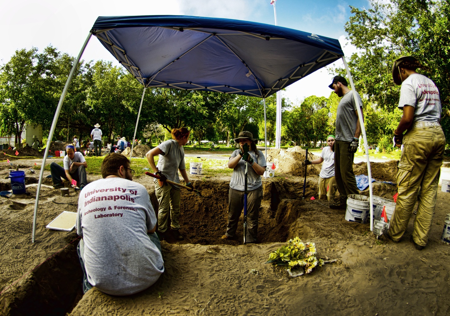 A burial covered with a sun tent with team members working in and around it