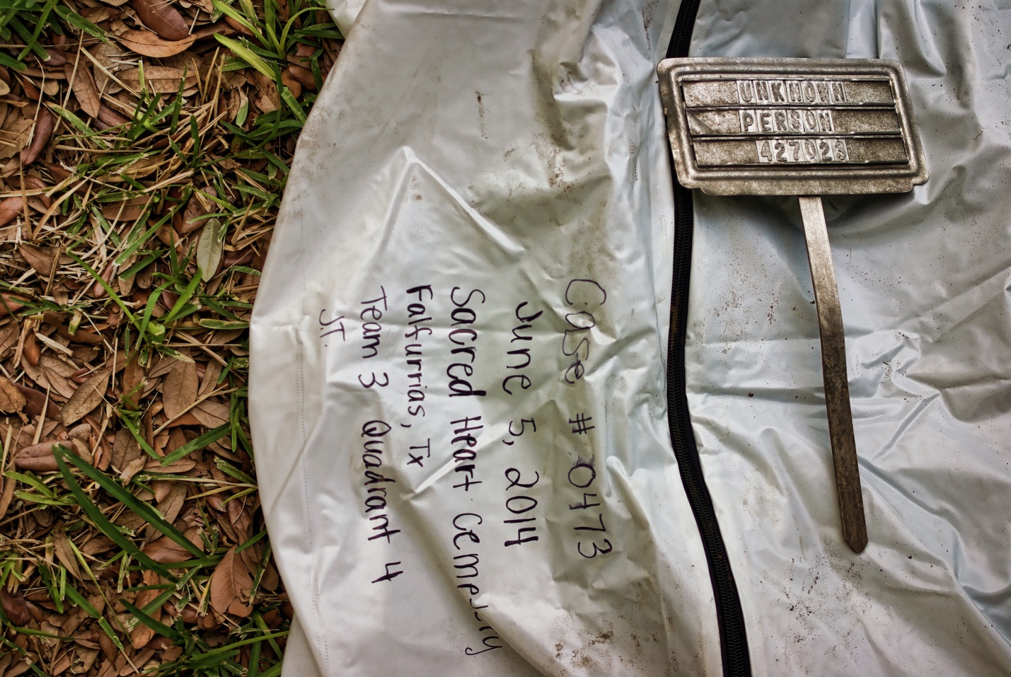 Upclose of the black writing on a body bag and a burial marker with "Unknown person" on it