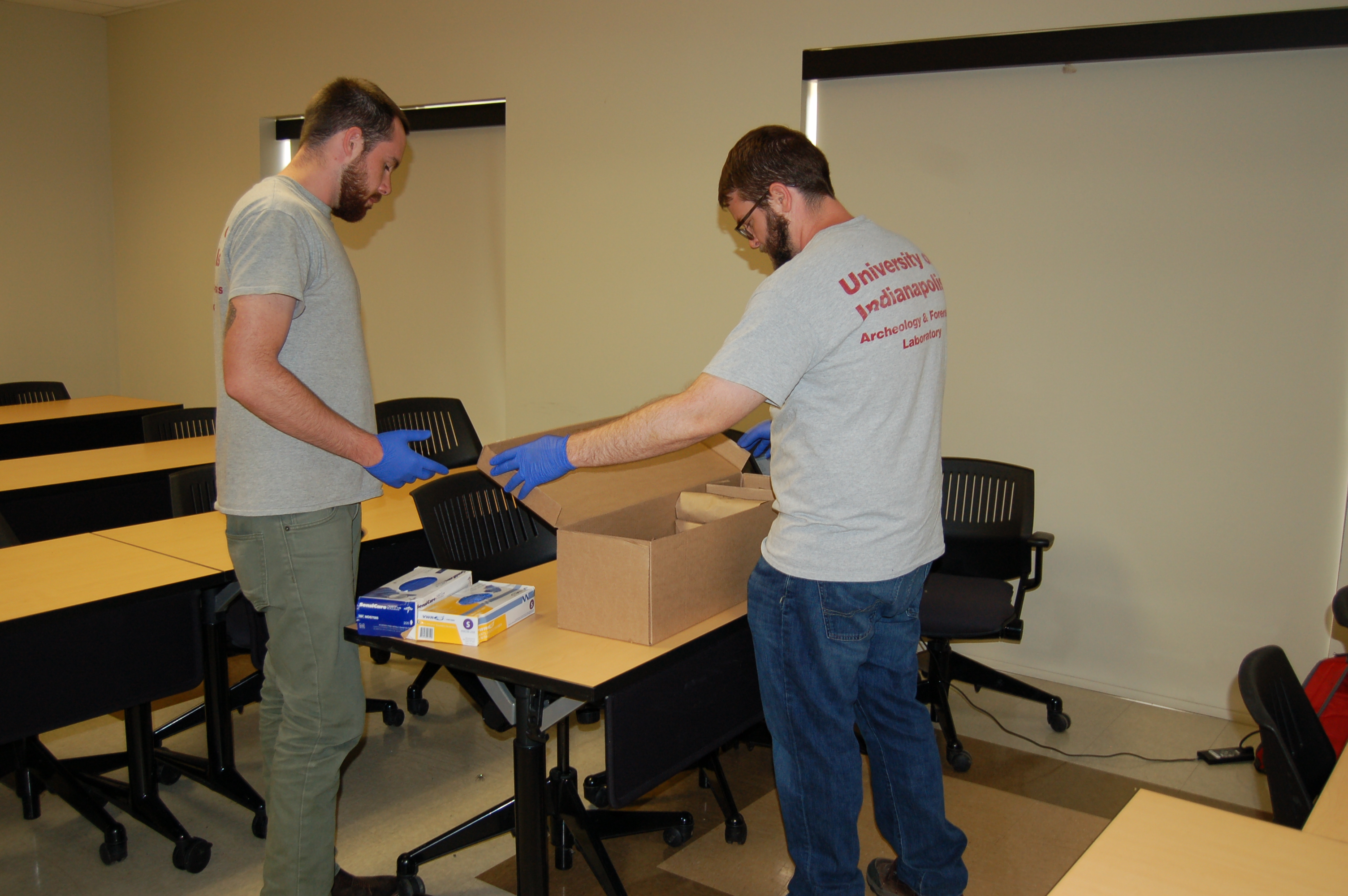 Two Beyond Borders Team Members opening a box with paper evidence bags within