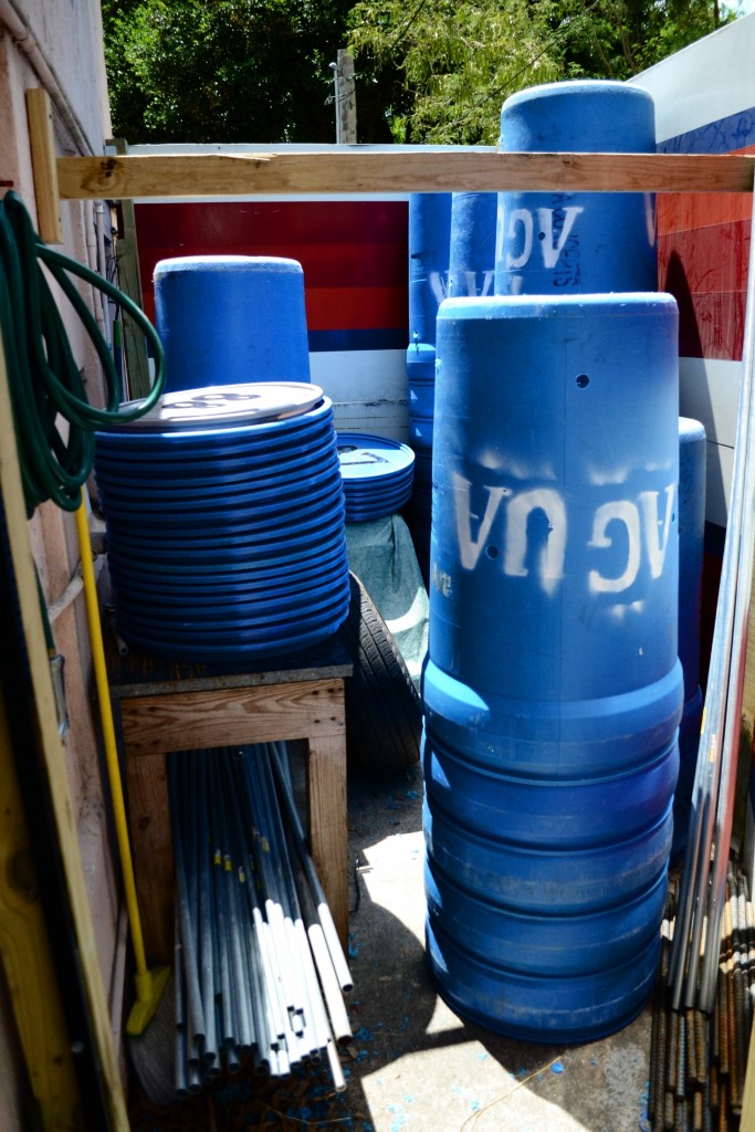 Stacks of water barrels, flagpoles, and barrel tops all organized in a storage area outdoors