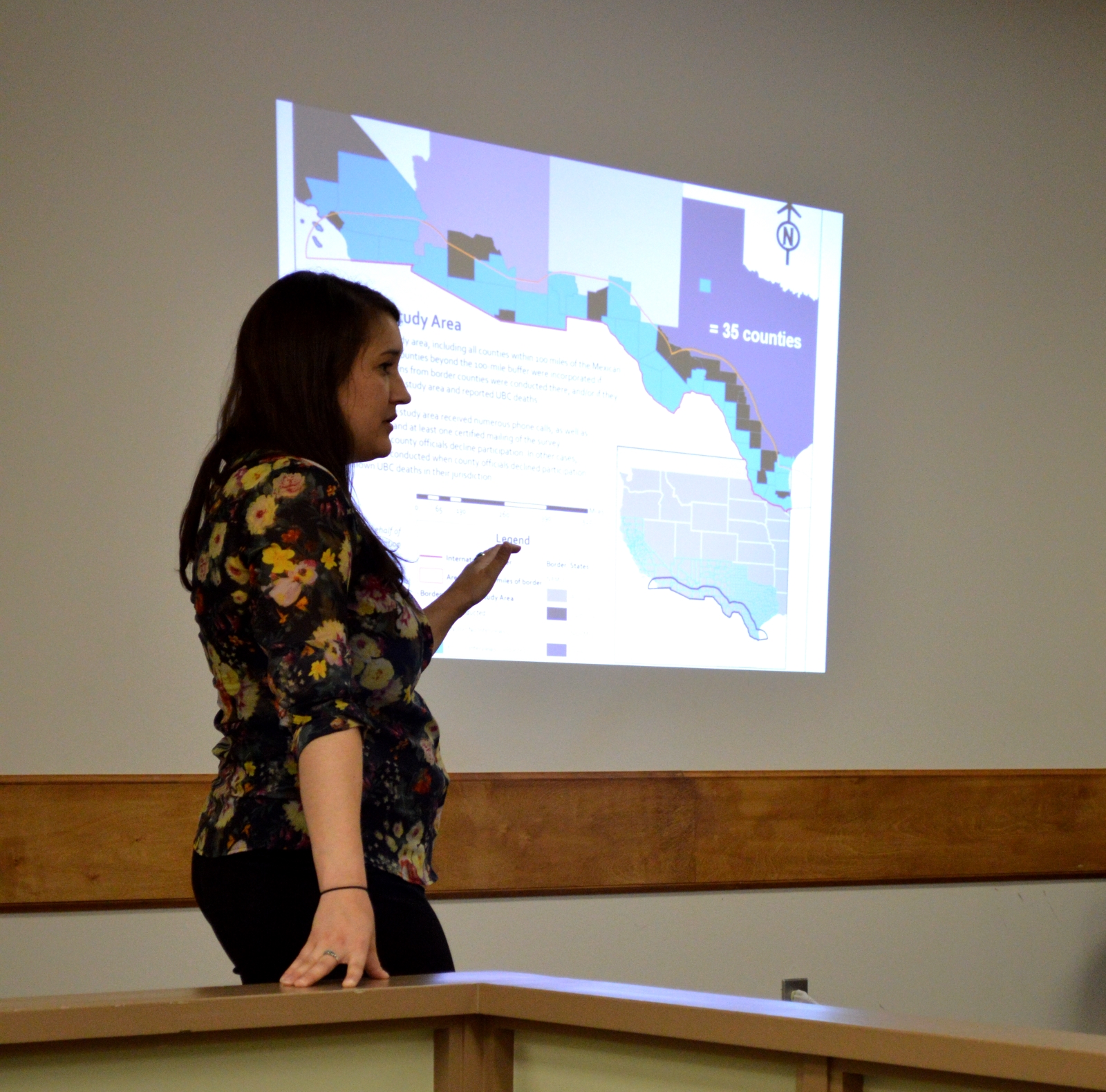 Hailey Duecker giving a presentation infront of a powerpoint depicting the Texas US border