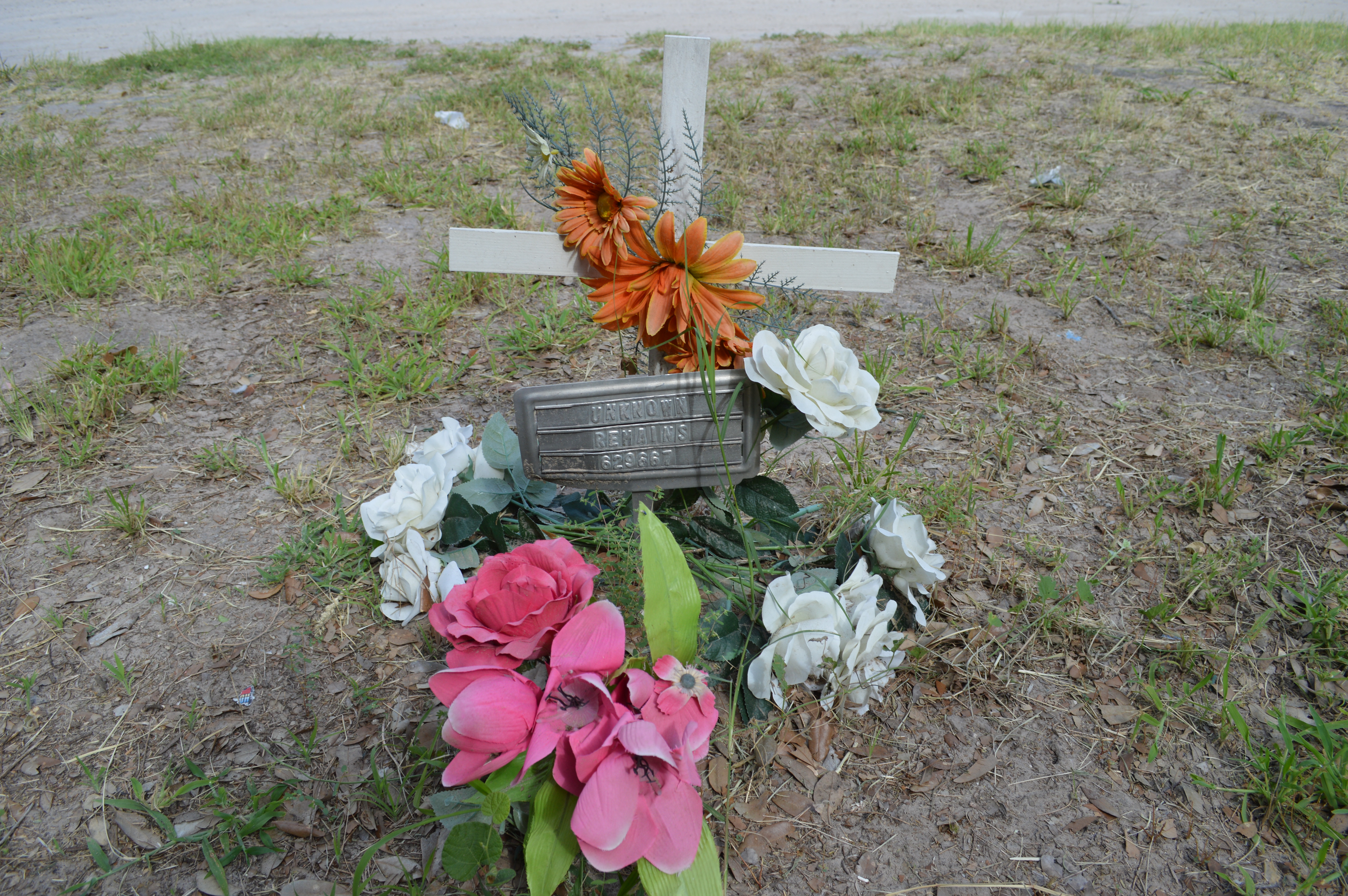 A cemetery marker labeled unknown remains with a white cross and colorful flowers added