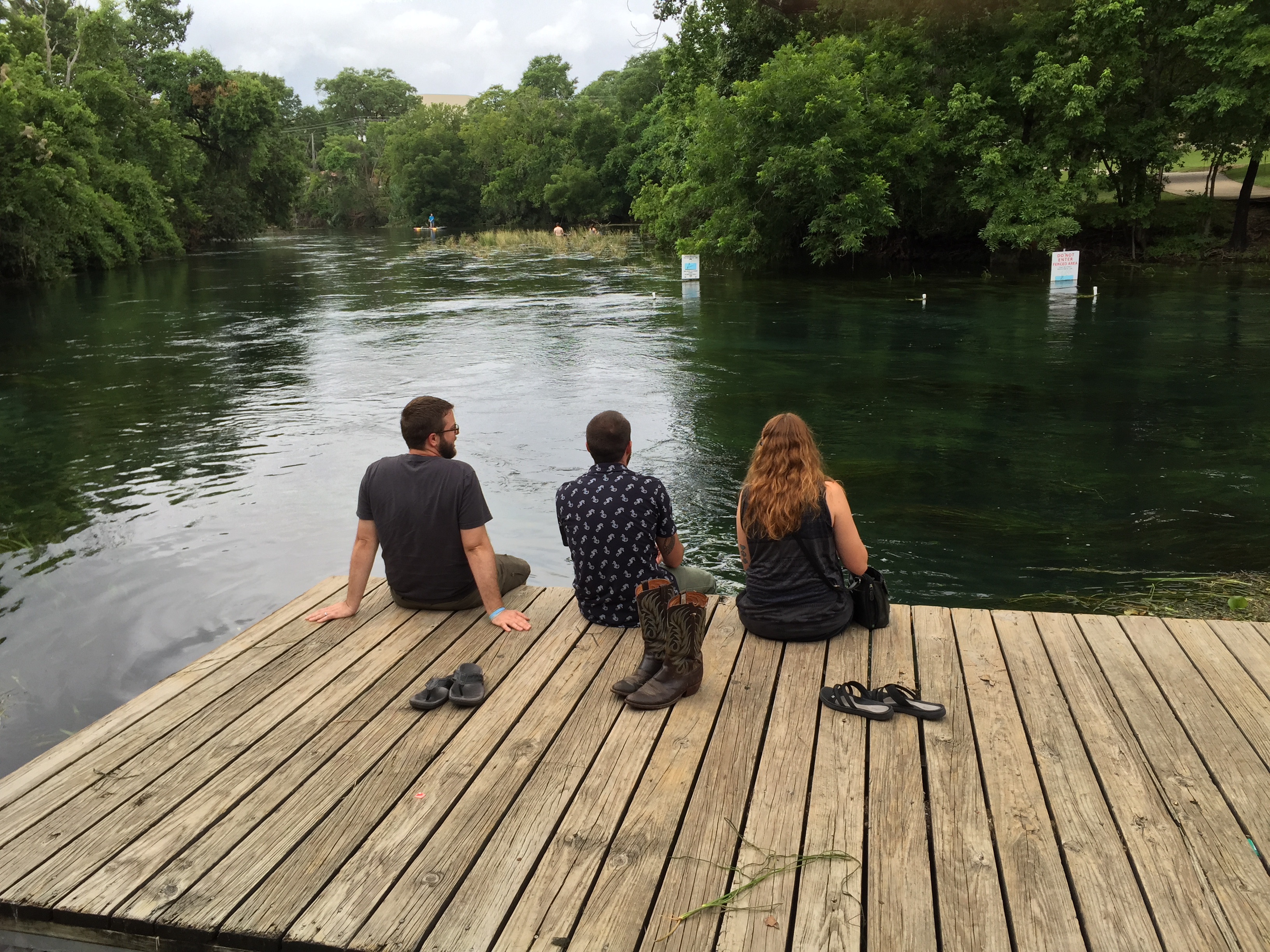 3 Beyond Borders team members siting on a dock, sitting their feet in the San Marcos River