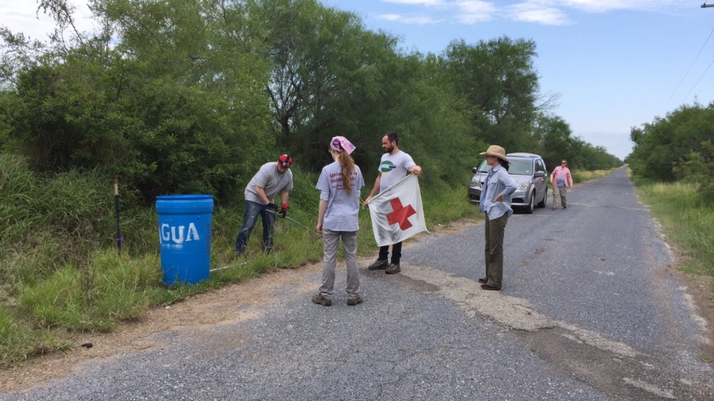Four team members placing a red cross flag on a blue barrel with aqua painted on it