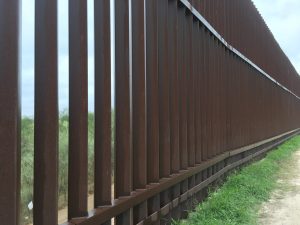 Looking along the rusty pillars of a border fence.