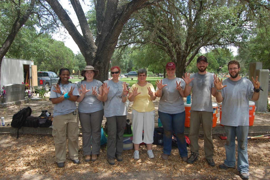 Group photo in dirty work clothes with Sister Pam, all holding 7 fingers up 