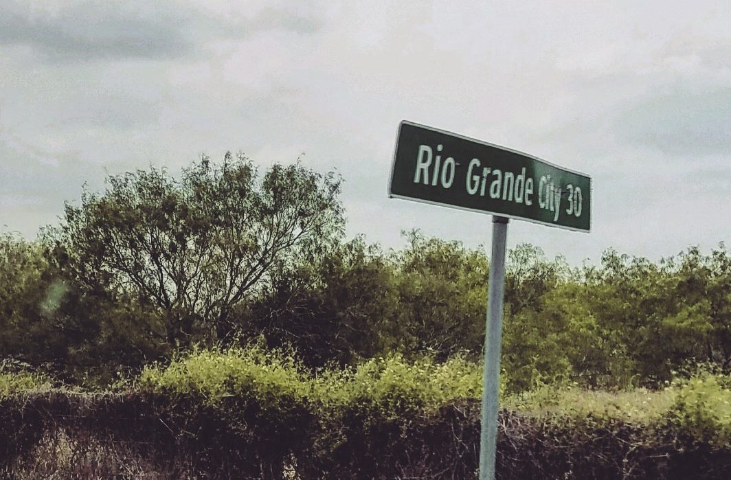 A street sign reading "Rio Grande City 30" in front of trees.