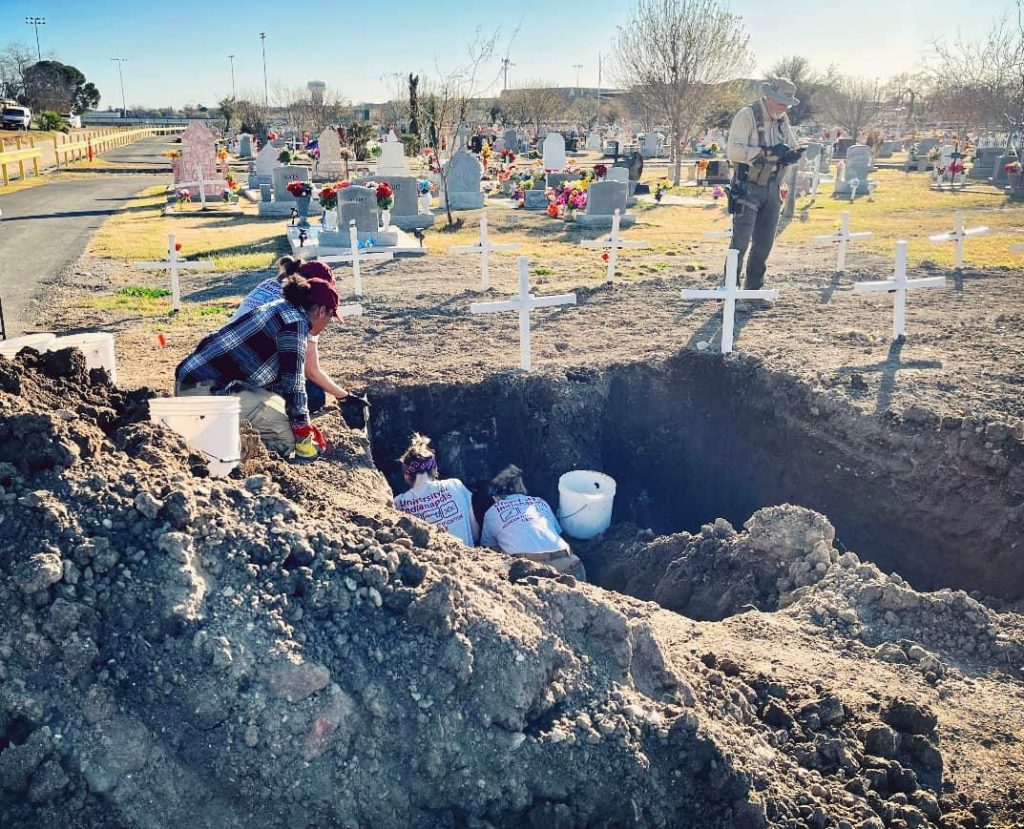 Team members exhuming a grave in Eagle Pass with Deputy White in the background.