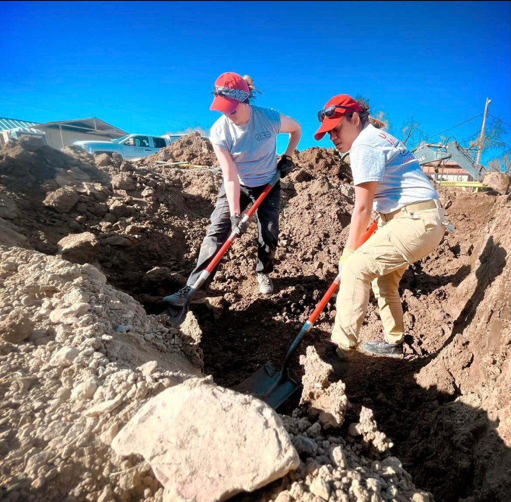 Two team members removing dirt from a burial with shovels.