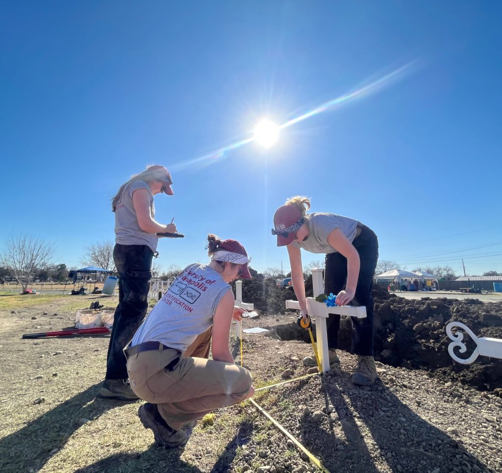 Three team members measuring the location of a grave marker to create a map.