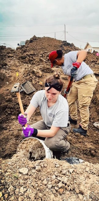 Two team members removing dirt from a burial with a shovel and mattock.