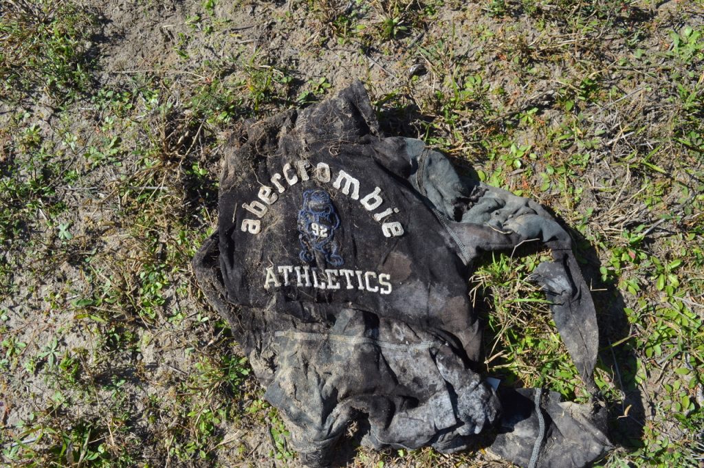 Black sweatshirt with dirt covering parts of it, laying in grass