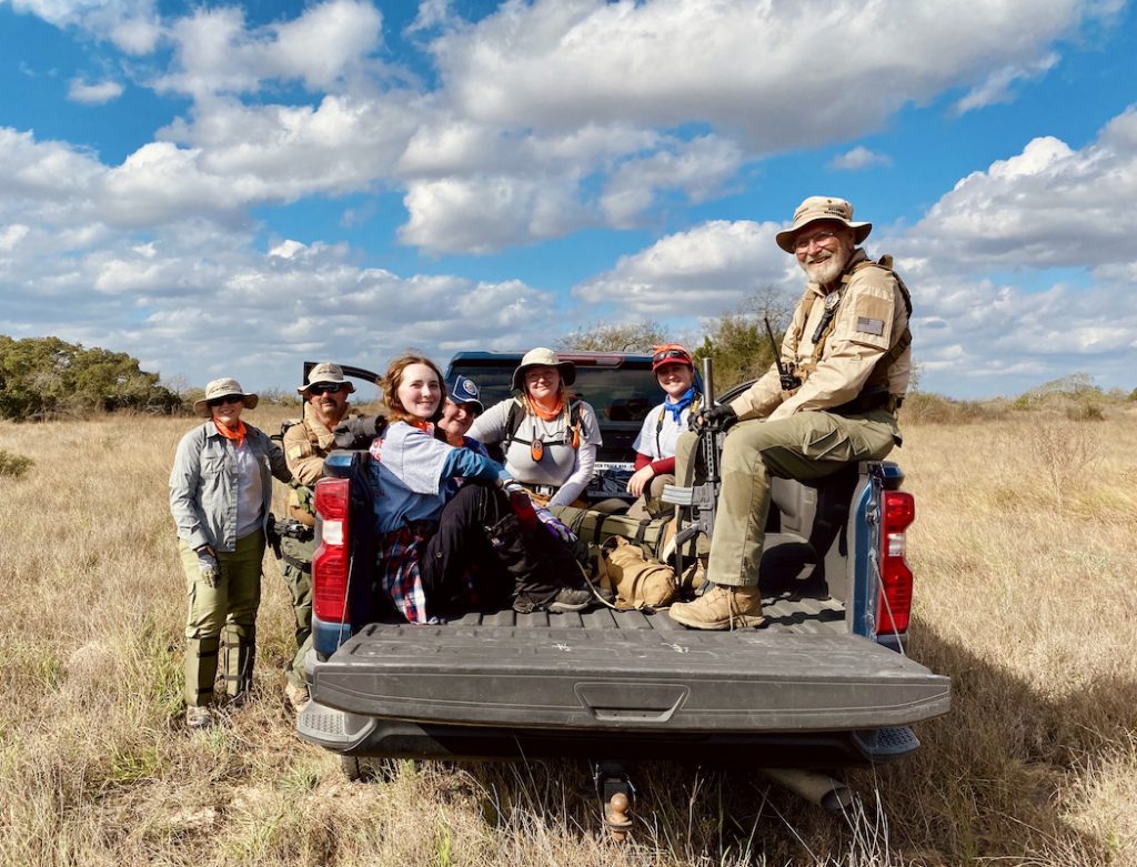 The team at the end of a day in the field, loading up in a truck to start the drive home. Five people sit in the back of a pick up truck bed while two stand to the left.