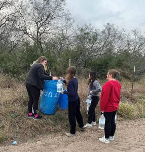 Beyond Borders Team members placing gallons of water into the blue barrel of the water station