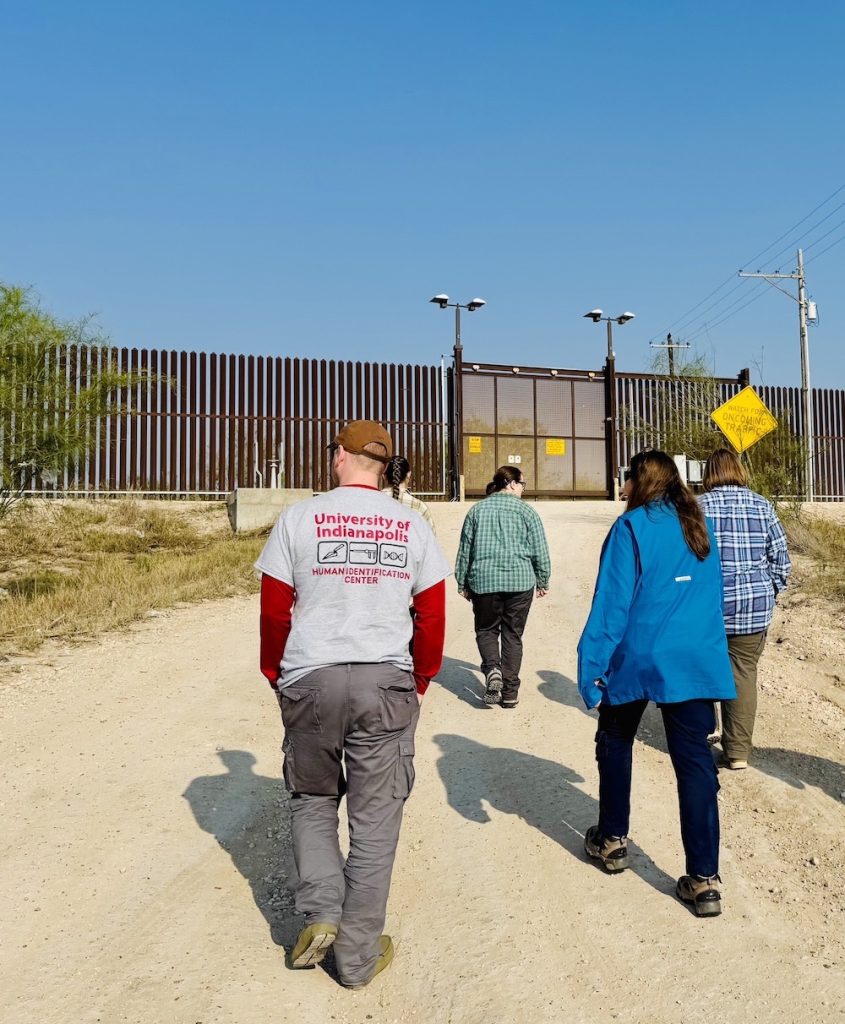 Dr. Latham walks up to the US-Mexico border wall the with the team