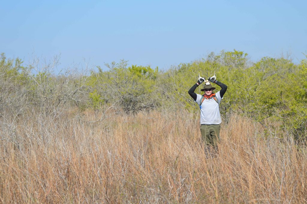 Reed holds up a partial deer skull with antlers to his head, mimicking a deer 